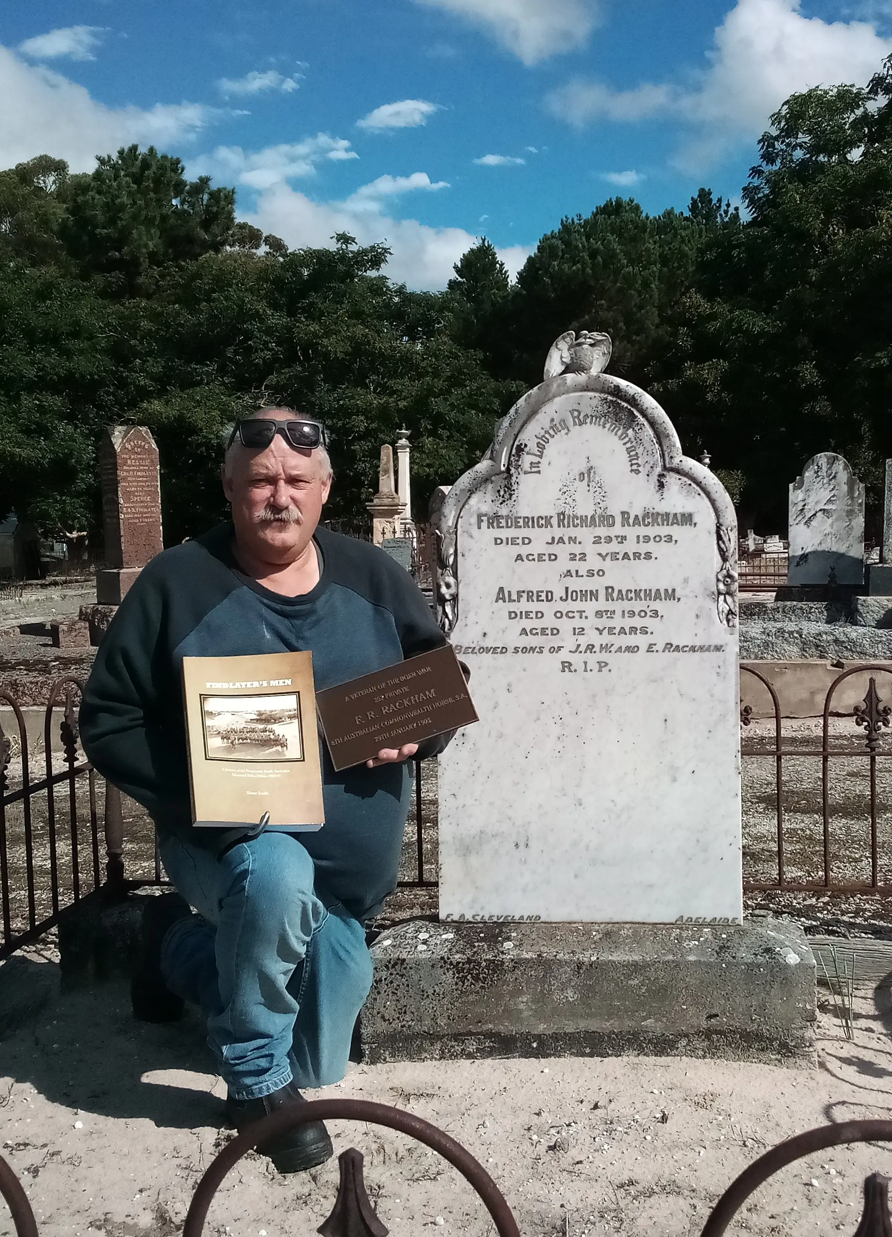 Shane Smith by the grave of Frederick Rackham, Naracoorte cemetery, holding a brass plaque supplied by the Office of Australian War Graves to commemorate his Boer War service. Shane Smith by the grave of Frederick Rackham, Naracoorte cemetery, holding a brass plaque supplied by the Office of Australian War Graves to commemorate his Boer War service.